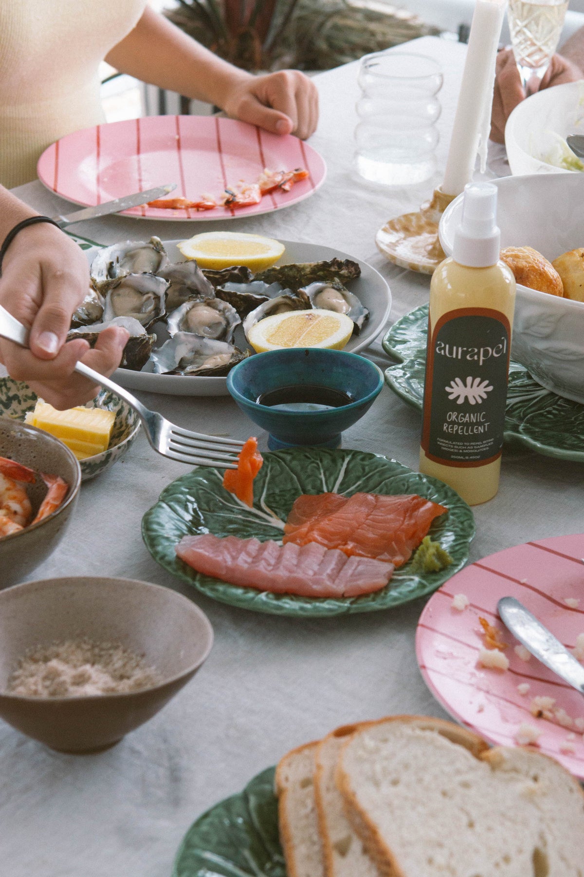A spray bottle of Aurapel organic repellent set amongst a dining table with seafood lunch